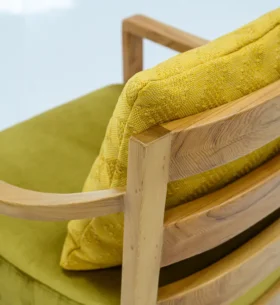 Close-up view of a wooden chair with curved armrests and back slats, featuring a green seat cushion and a textured yellow pillow.