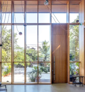 Interior space with floor-to-ceiling wood-framed windows and a tall wood entry door, bringing natural light and views of surrounding greenery into the building.