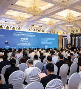 Attendees seated in a conference hall listening to a speaker at a large international building industry forum, with presentation screens displaying multilingual content.