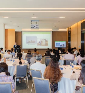 Participants attend a seminar on wood products and manufacturing, with a presenter speaking beside a screen displaying technical information and product examples.