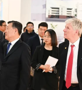 Delegates tour an exhibition on construction and building development, viewing displays and presentation materials related to building projects and wood construction.