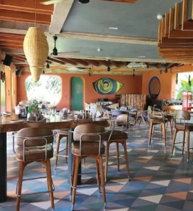 Restaurant interior featuring exposed wood beams and ceiling elements, wood furnishings and a colourful geometric tile floor, with tables set for dining.