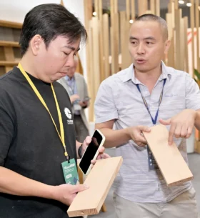 Two attendees examine and compare wood product samples at an industry trade show, discussing material characteristics while standing in front of a wood display
