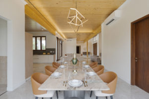 Dining area view from head of the table, with silverware and dining ware set, an accent chandelier, and bright wooden ceiling.