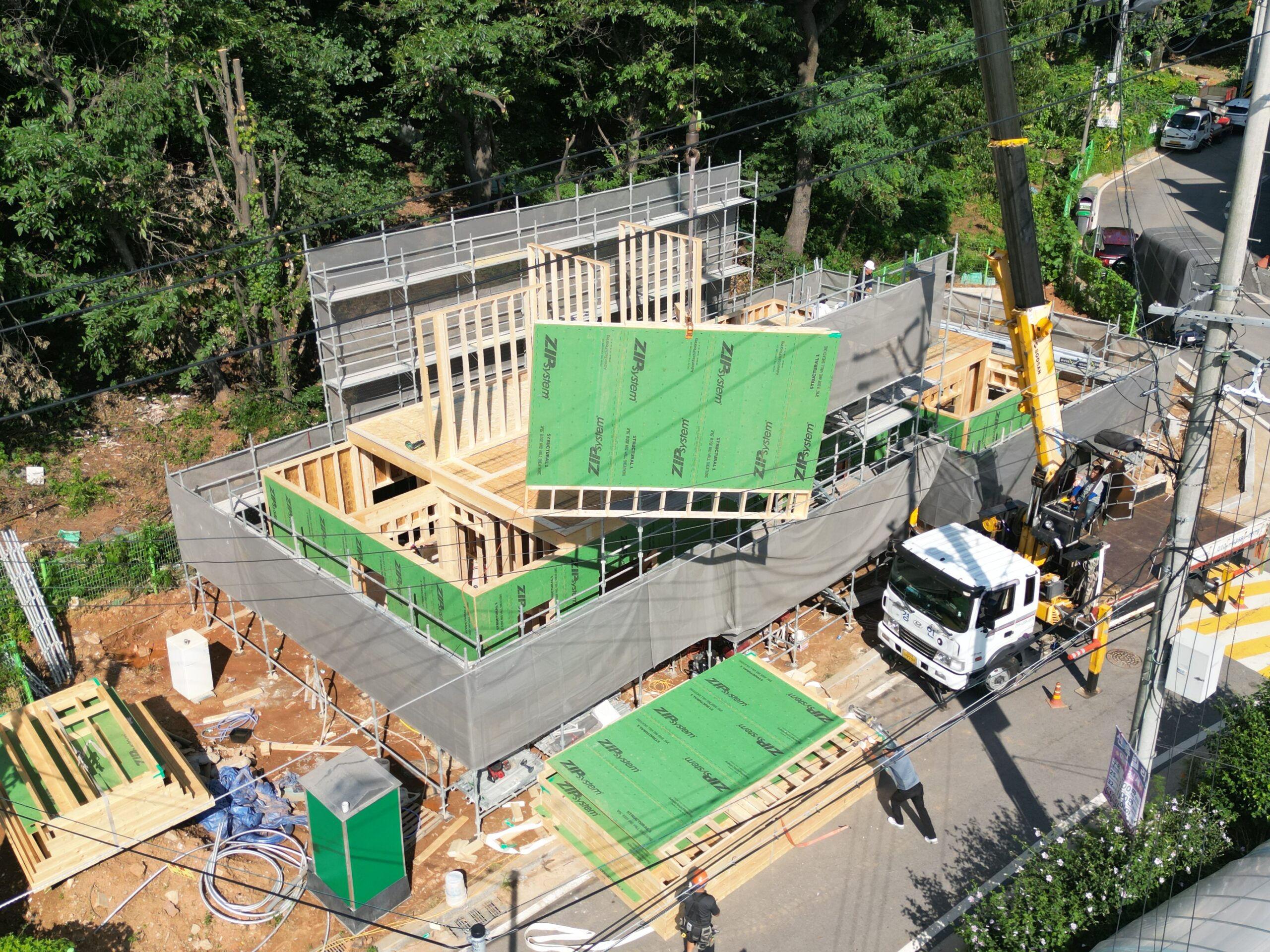 Closer aerial view to the detached home being built. A crane lifts up a large, prefabricated component into place.