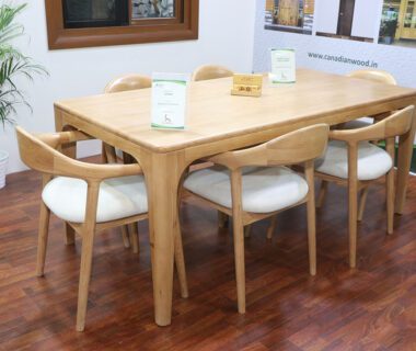 A close-up of a light-colored wooden dining table with six matching chairs with white upholstered seats, displayed in a showroom setting.