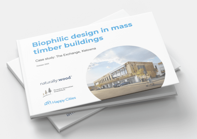 Stack of printed reports titled “Biophilic design in mass timber buildings,” featuring a case study of The Exchange in Kelowna. The cover shows a circular photo of a modern, two-storey mass timber building with wood cladding and large windows, set along a street with a vehicle and a passing cyclist. Logos for naturally:wood, Forestry Innovation Investment, and Happy Cities appear at the bottom, with “October 2025” noted beneath the subtitle.