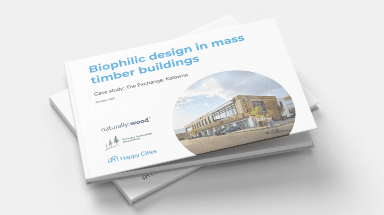 Stack of printed reports titled “Biophilic design in mass timber buildings,” featuring a case study of The Exchange in Kelowna. The cover shows a circular photo of a modern, two-storey mass timber building with wood cladding and large windows, set along a street with a vehicle and a passing cyclist. Logos for naturally:wood, Forestry Innovation Investment, and Happy Cities appear at the bottom, with “October 2025” noted beneath the subtitle.