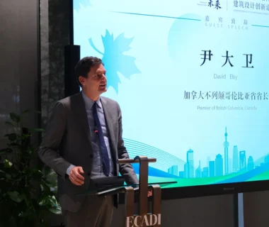 Premier David Eby delivers a speech at the East China Architectural Design & Research Institute (ECADI), standing at a podium beside a presentation screen displaying his name and title, Premier of British Columbia, Canada.