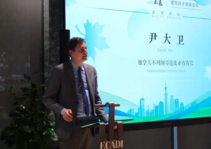 Premier David Eby delivers a speech at the East China Architectural Design & Research Institute (ECADI), standing at a podium beside a presentation screen displaying his name and title, Premier of British Columbia, Canada.