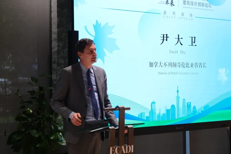 Premier David Eby delivers a speech at the East China Architectural Design & Research Institute (ECADI), standing at a podium beside a presentation screen displaying his name and title, Premier of British Columbia, Canada.