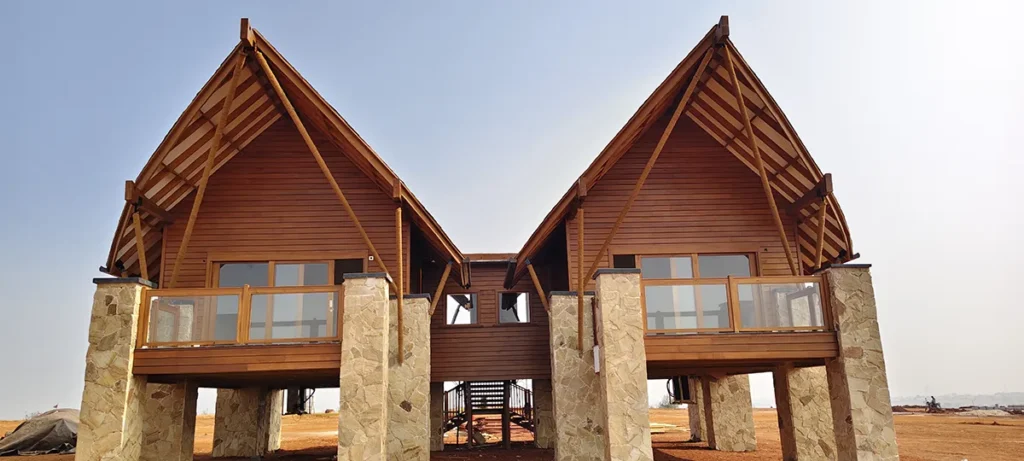 Elevated wood-clad villas with exposed timber roof framing, wood siding, wood decking and wood-framed railings supported by stone columns.