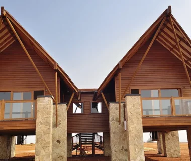 Elevated wood-clad villas with exposed timber roof framing, wood siding, wood decking and wood-framed railings supported by stone columns.