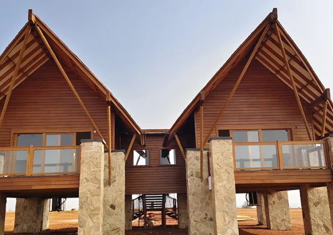 Elevated wood-clad villas with exposed timber roof framing, wood siding, wood decking and wood-framed railings supported by stone columns.