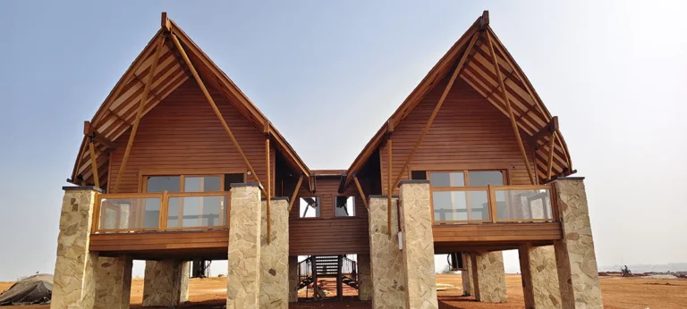 Elevated wood-clad villas with exposed timber roof framing, wood siding, wood decking and wood-framed railings supported by stone columns.