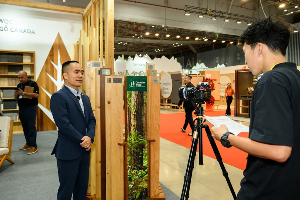 FII Vietnam Country Director participates in a media interview at a Canadian Wood exhibition booth, with wood products displayed in the background.