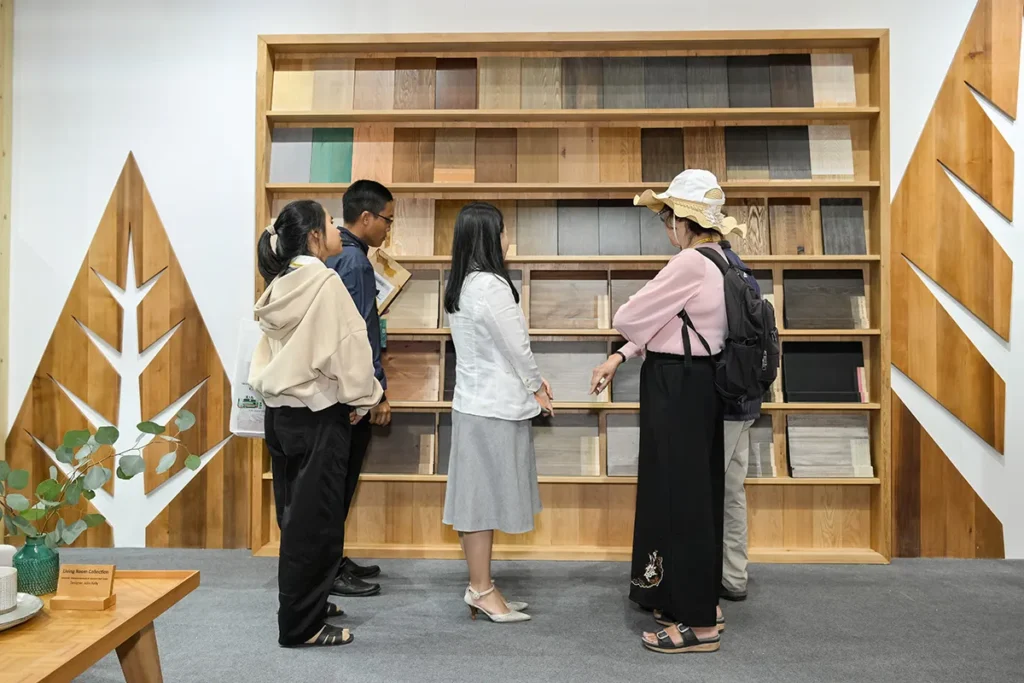 Visitors examine wood finishing samples displayed on a feature wall at a Canadian Wood exhibition booth.