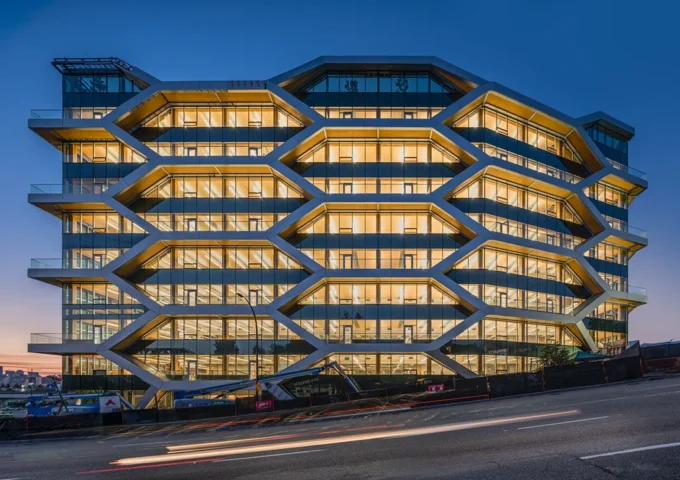 Office building with a distinctive geometric façade that highlights exposed mass timber structure and floor plates behind glass walls.